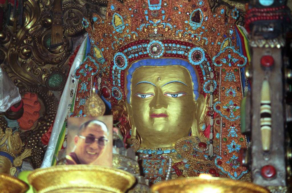 01-1 Shakyamuni Buddha In Jokhang Temple The Chapel of Jowo Shakyamuni in Lhasaa Jokhang Temple is the most important shrine in Tibet, housing a 1.5m sitting image of Shakyamuni at the age of 12. It is supposedly one of only three made during his lifetime. It was a gift from the Chinese Princess Wencheng to her husband King Songtsen Gampo. The Jowo sits on a majestic massive three-tiered stone platform. Two silver-plated dragons presented by the Chinese emperor entwine the ornate pillars that support an intricate double canopy over the Jowo. An ornate crown of coral, turquoise, diamonds, rubies, and other precious gems, sits on the Jowos head. Note the photo of the current 14th Dalai Lama, allowed in Tibet when I took this photo in 1993.